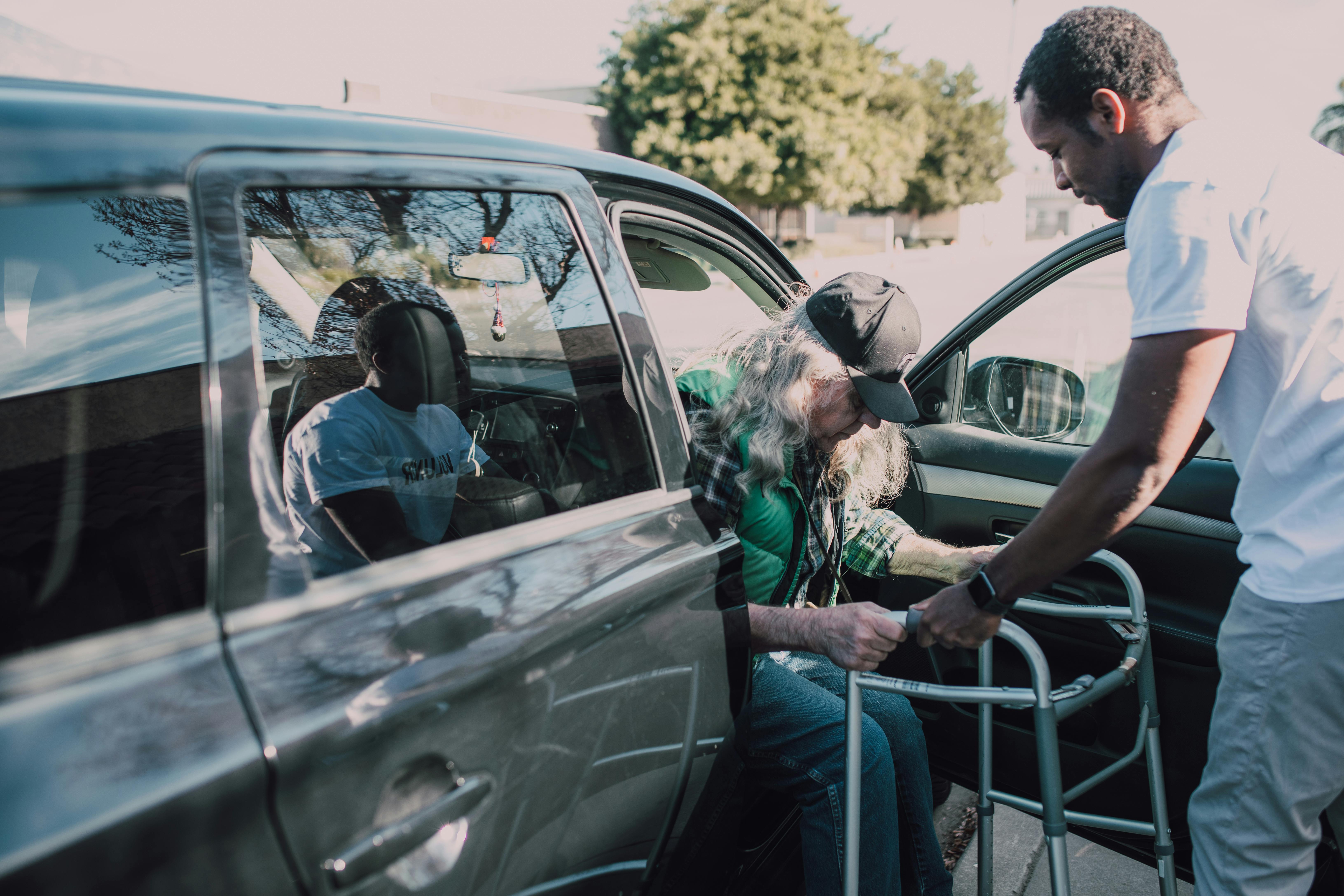 Elderly man with a walker being assisted exiting a vehicle